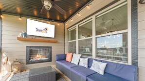 Un espacio al aire libre acogedor con chimenea, un sofá azul y una pantalla de televisión que muestra 'Sunset Nightly Rentals'.