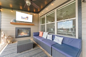 Un espacio al aire libre acogedor con chimenea, un sofá azul y una pantalla de televisión que muestra 'Sunset Nightly Rentals'.