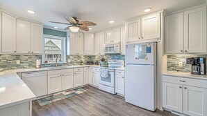 Una cocina moderna con armarios blancos, microondas, refrigerador y ventilador de techo.