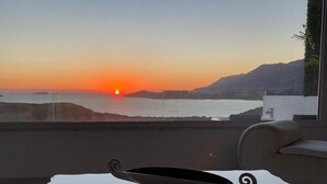 Une vue sur le coucher de soleil depuis un balcon, avec une table en verre, un verre de whisky et un canapé moderne.