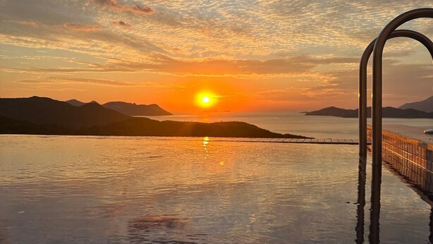 Une piscine à débordement offrant une vue imprenable sur le coucher de soleil, la mer et les montagnes.