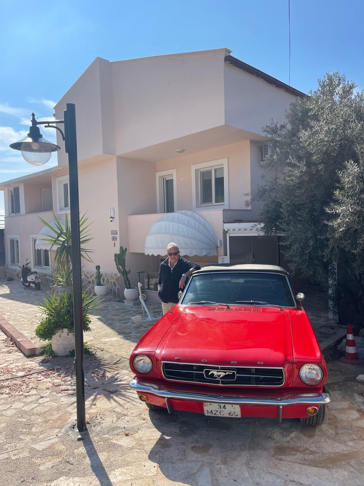 A red vintage car parked in front of a building with a white facade and a large umbrella.