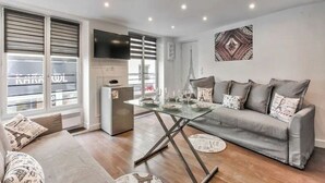 Un salon moderne avec un canapé gris, une table basse en verre et un téléviseur à écran plat fixé au mur.