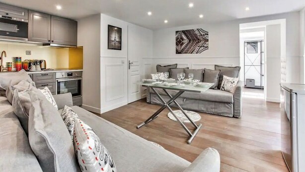 Un salon moderne avec un canapé, une table à manger dressée pour quatre personnes et une cuisine en arrière-plan.