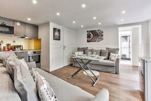 Una sala moderna con un sofá, una mesa de comedor para cuatro personas y una cocina al fondo.