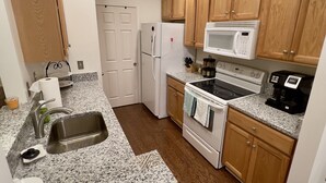 Una cocina compacta con encimeras de granito, gabinetes de madera, un refrigerador blanco, un microondas, un horno y una cafetera.
