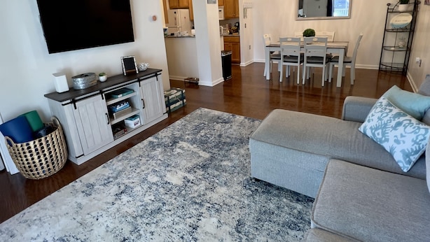 Una sala de estar moderna con televisor de pantalla plana, sofá gris y un comedor con mesa y sillas blancas.