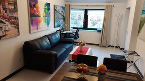 A modern living room with a black leather sofa, a dining table with a red table runner, and a window with curtains.
