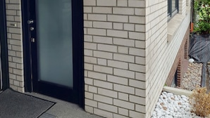 A building with a brick exterior, a black door, and a small outdoor area with gravel and plants.