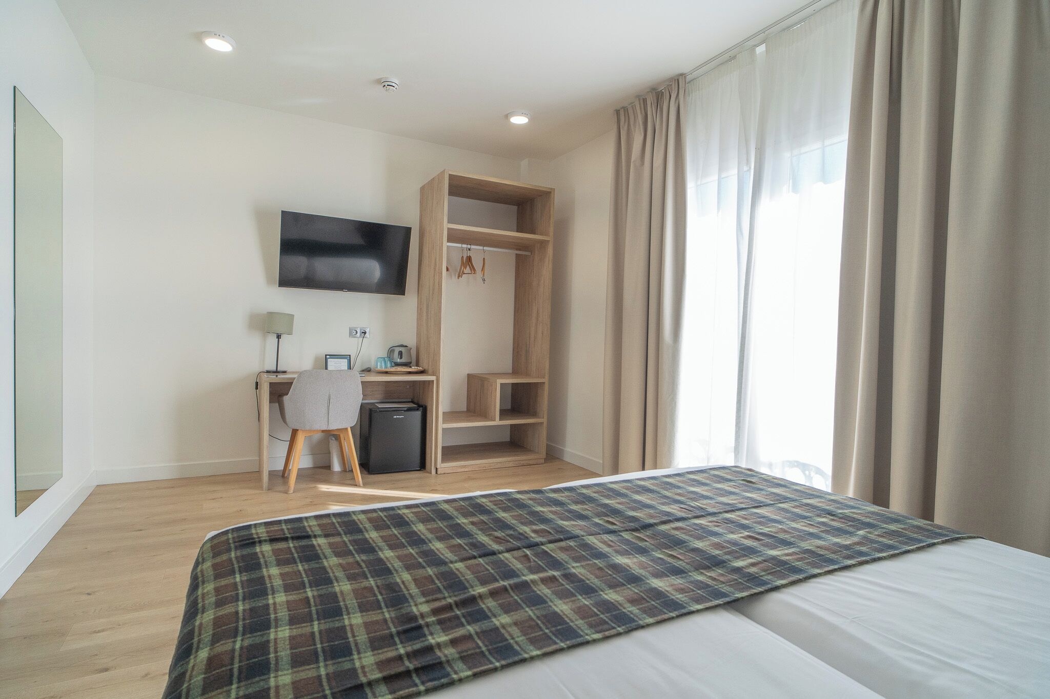 A hotel room with a bed, a desk with a chair, a television, and a wardrobe.