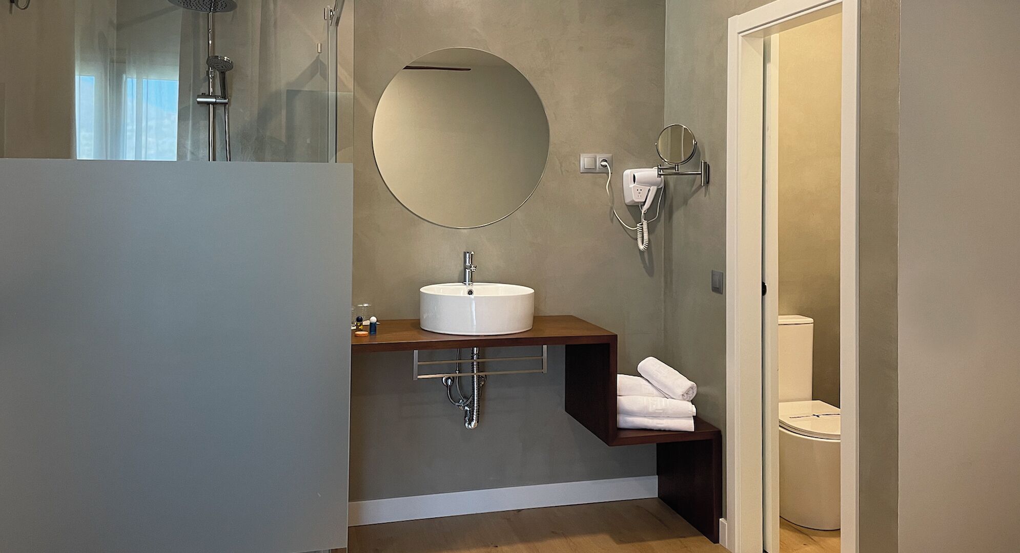 Un baño moderno con un espejo redondo, un lavabo, un perchero para toallas y una ducha.