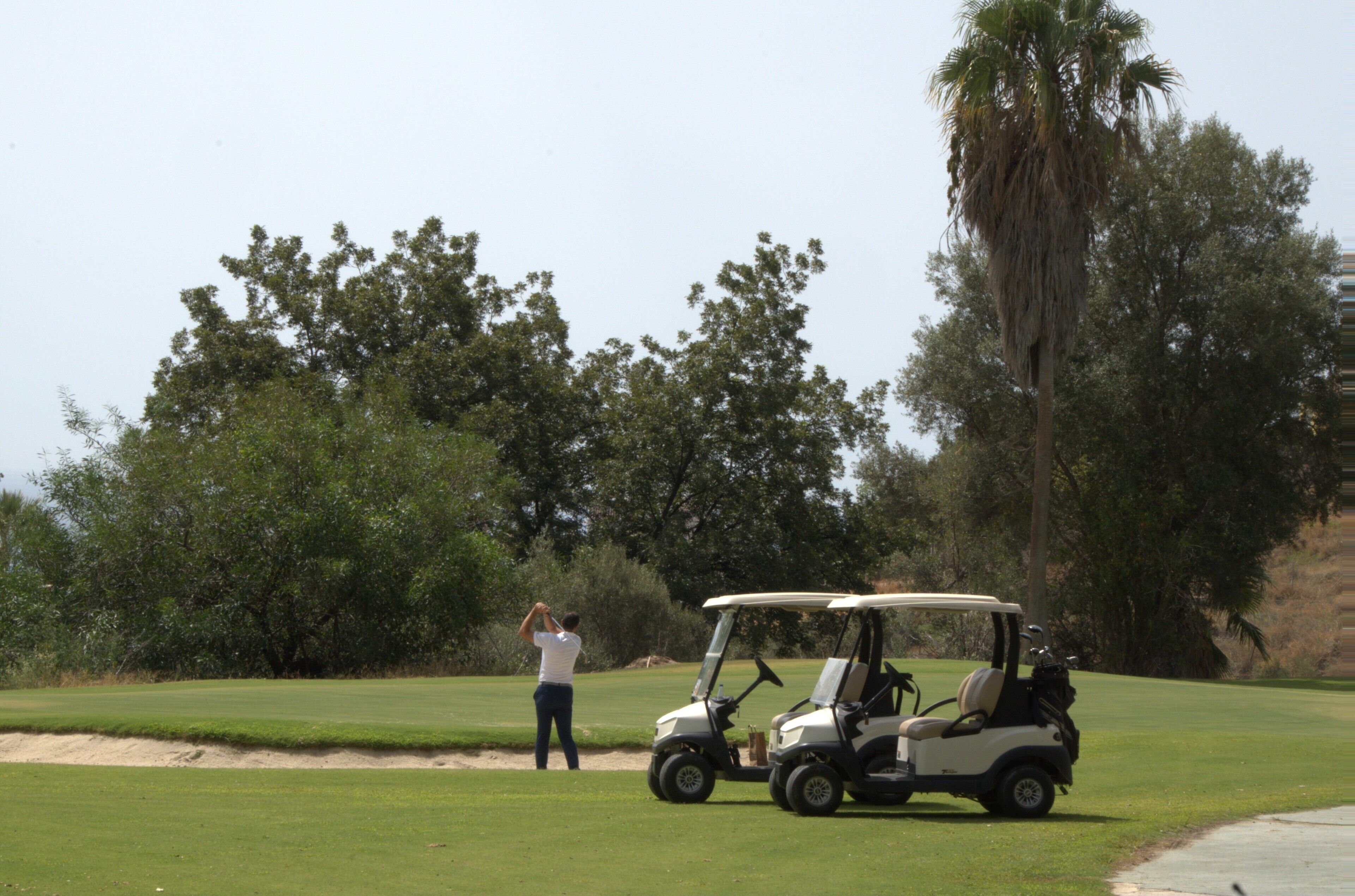 Campo de golf con un carrito de golf y una persona a punto de golpear la pelota.