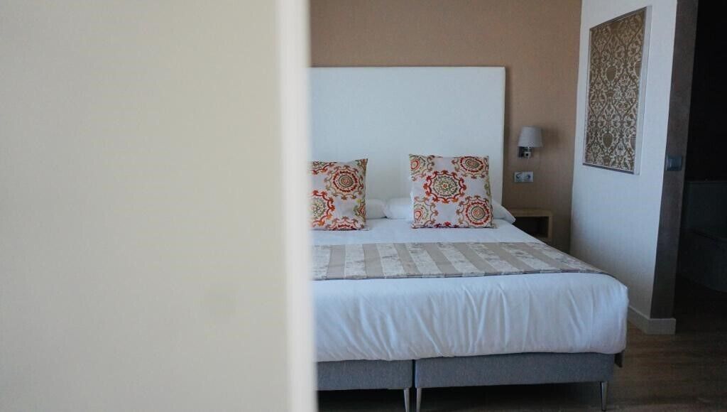 A neatly made bed with patterned pillows, a bedside lamp, and a decorative wall piece.