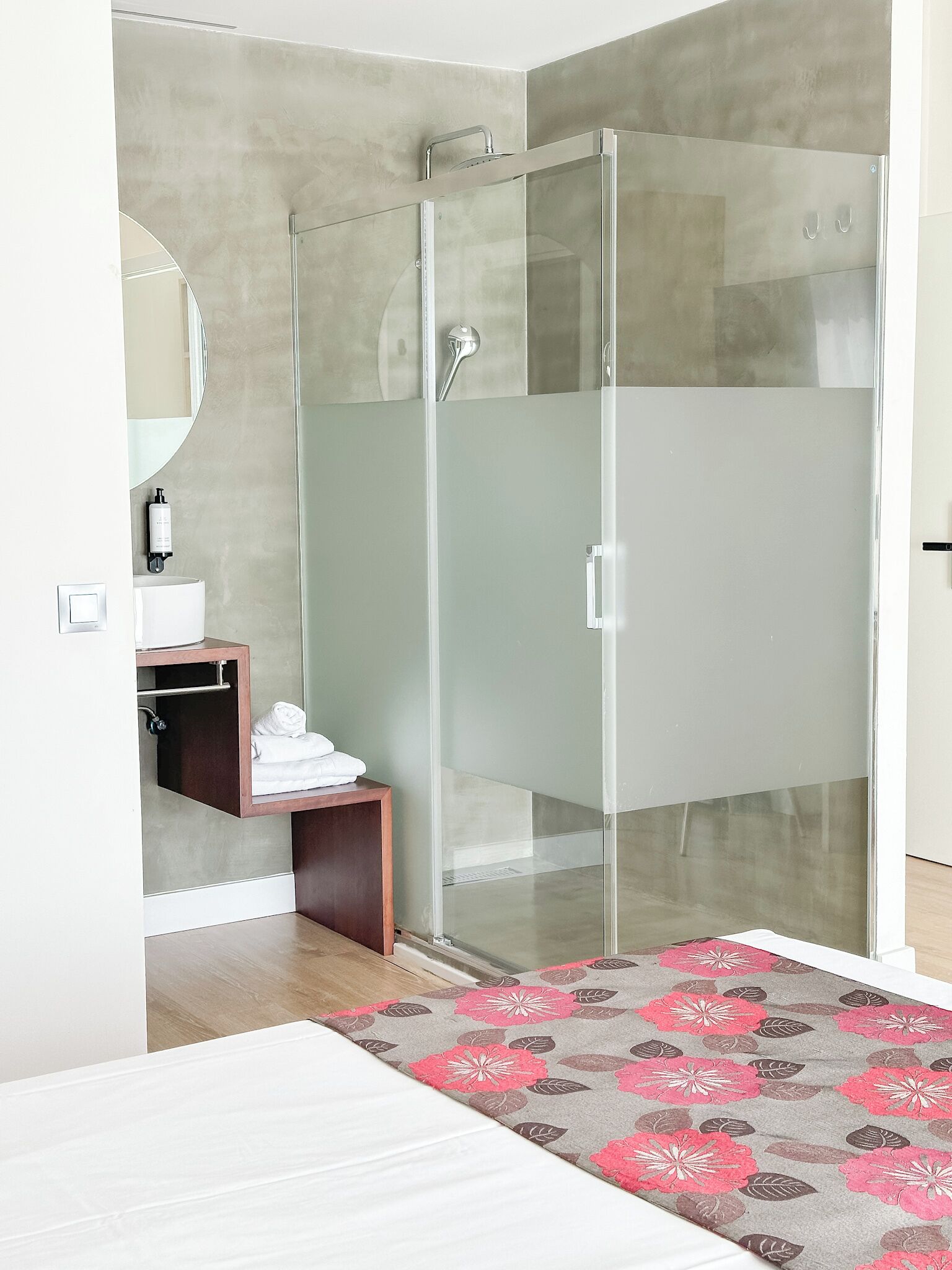 A modern bathroom with a glass shower enclosure, a wooden vanity, a mirror, and a patterned rug.