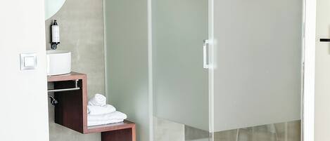A modern bathroom with a glass shower enclosure, a wooden vanity, a mirror, and a patterned rug.