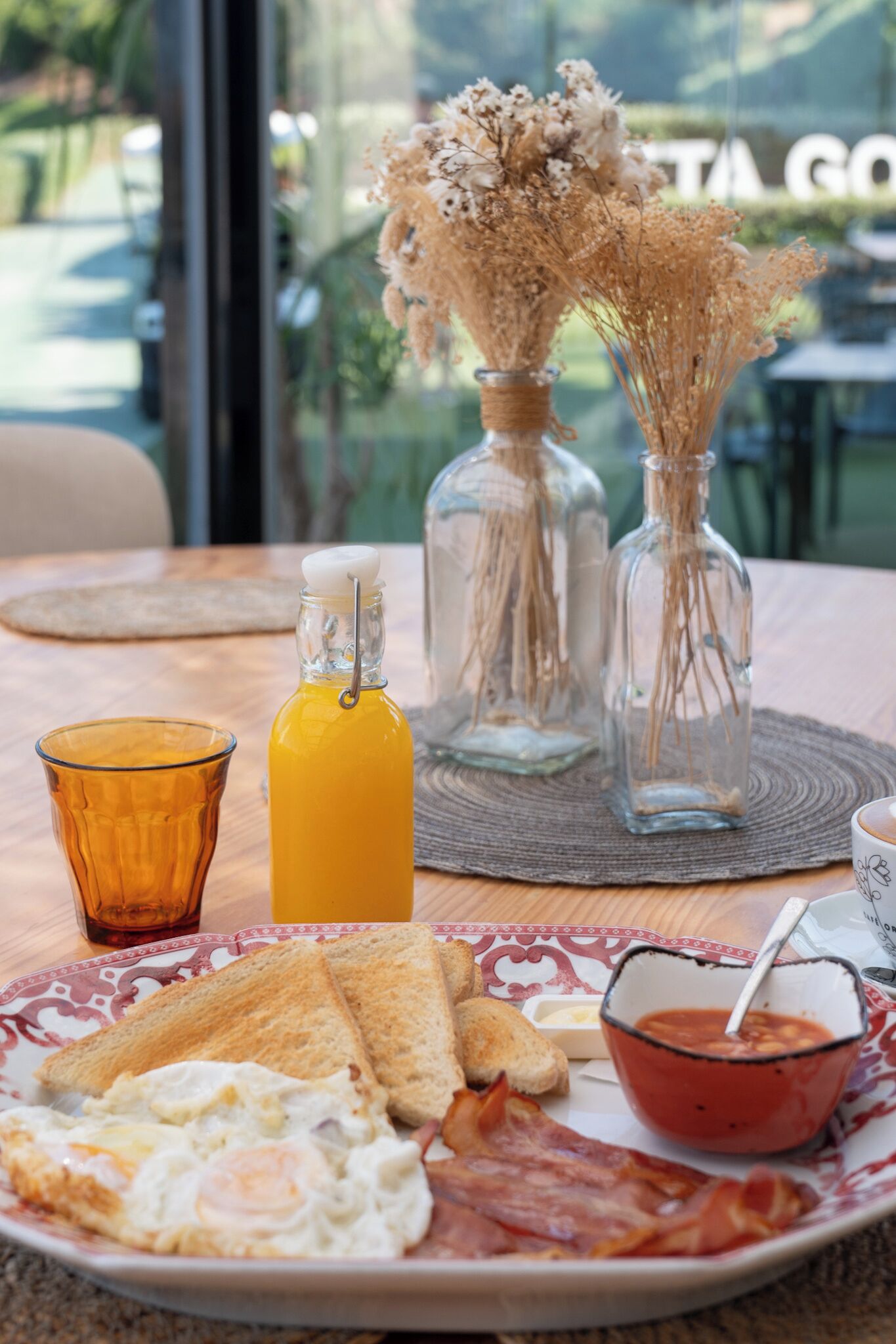 Desayuno con tostadas, huevos, tocino, un vaso de jugo de naranja y un tazón de sopa de tomate.