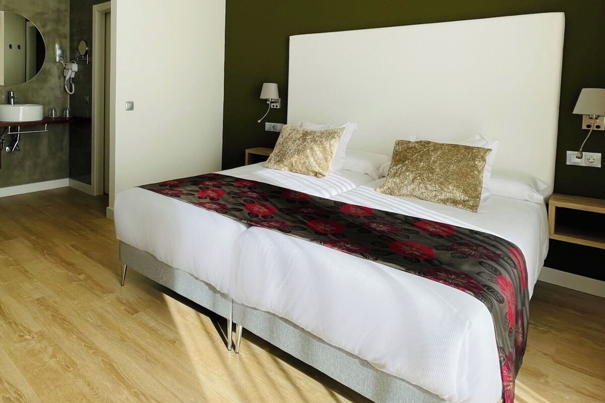 A bedroom with a bed, bedside tables, a mirror, a shower area, and a sink.