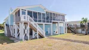 Une maison à deux étages située en bord de mer, dotée d’un porche couvert, d’un escalier et d’une petite terrasse.