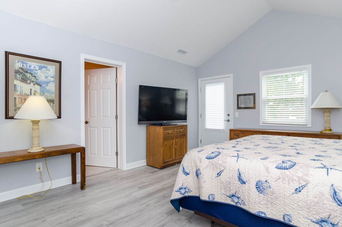 A bedroom with a bed, a television, a wooden bench, and a framed picture on the wall.