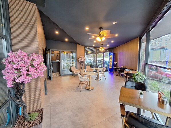 A modern cafe interior with seating, a ceiling fan, and a vending machine. - N'Ala Otel (Erenler)