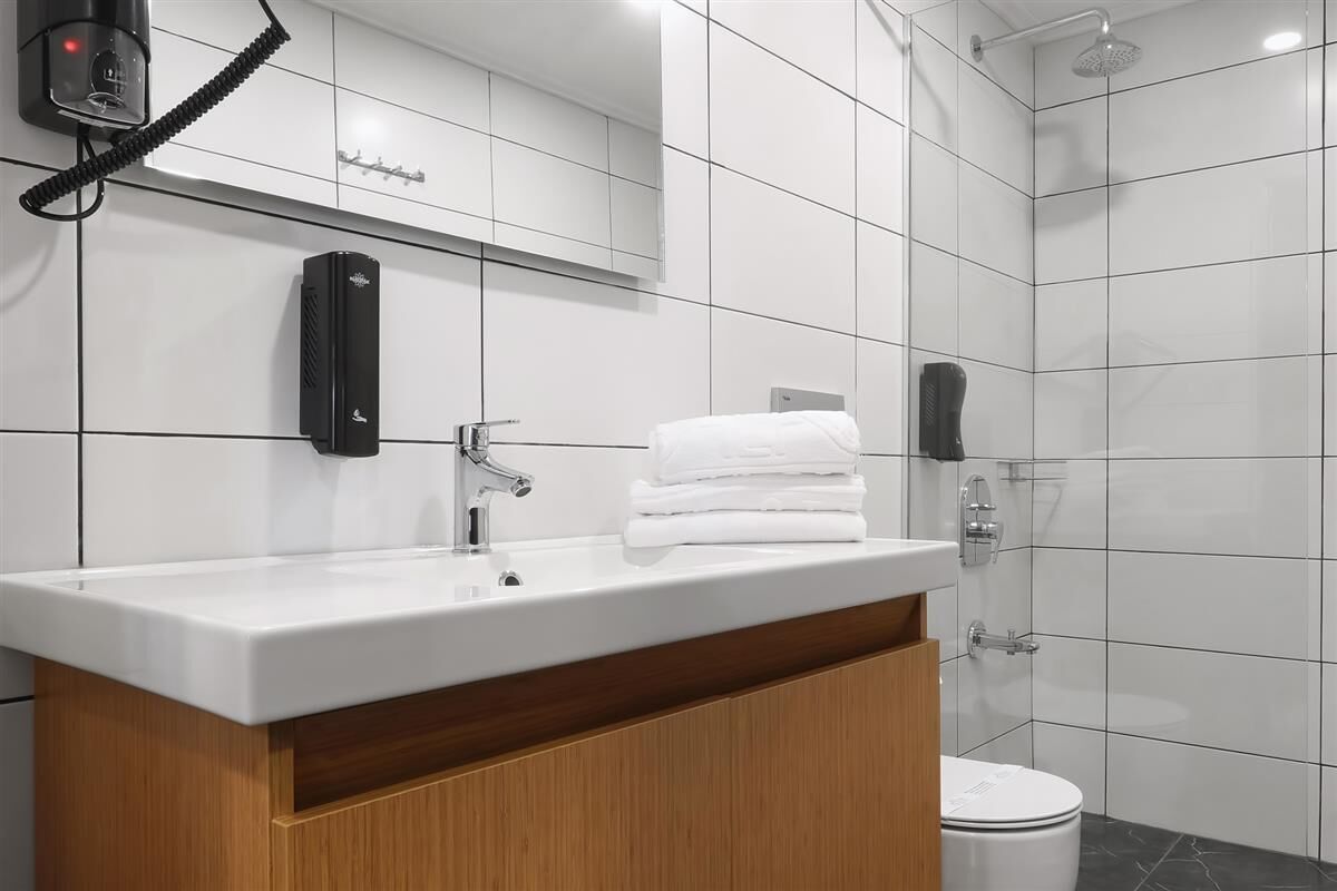 Une salle de bain moderne avec un lavabo blanc, un miroir, un porte-serviettes et un espace douche.