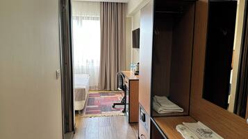 A hotel room with a bed, a desk with a computer, a wardrobe, and a bathroom visible through an open door.