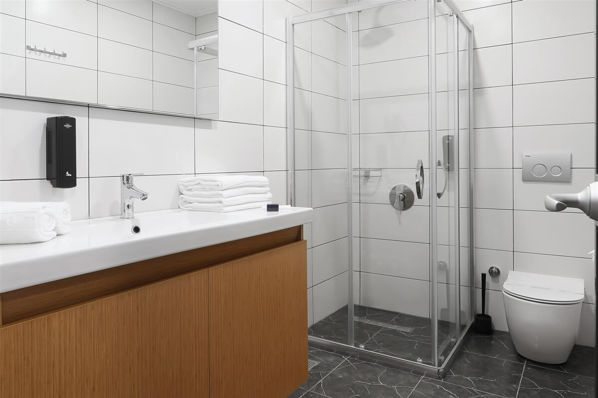 A modern bathroom with a glass-enclosed shower, a white sink with a wooden cabinet, and a toilet.
