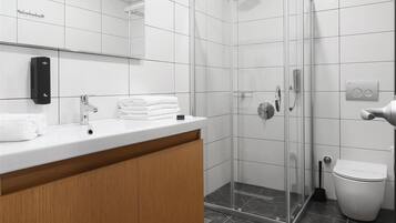 Un baño moderno con ducha de vidrio, un lavamanos blanco con mueble de madera y un inodoro.