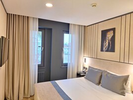 Una habitación de hotel con cama, cortinas, un cuadro y una mesita de noche.