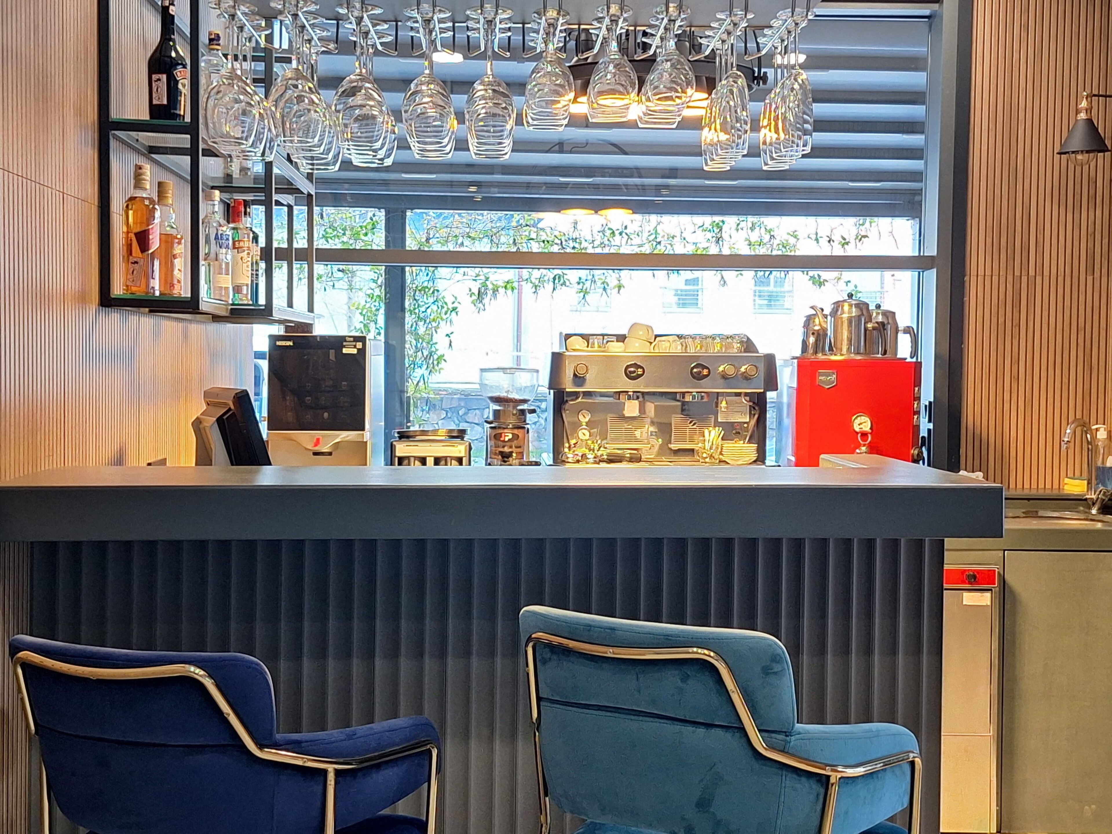 Uma área de bar com dois banquetes azuis, uma máquina de café e uma garrafa de vinho na estante.