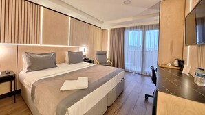 Una habitación de hotel moderna con una cama grande, un escritorio, una silla, un televisor y vistas al exterior.