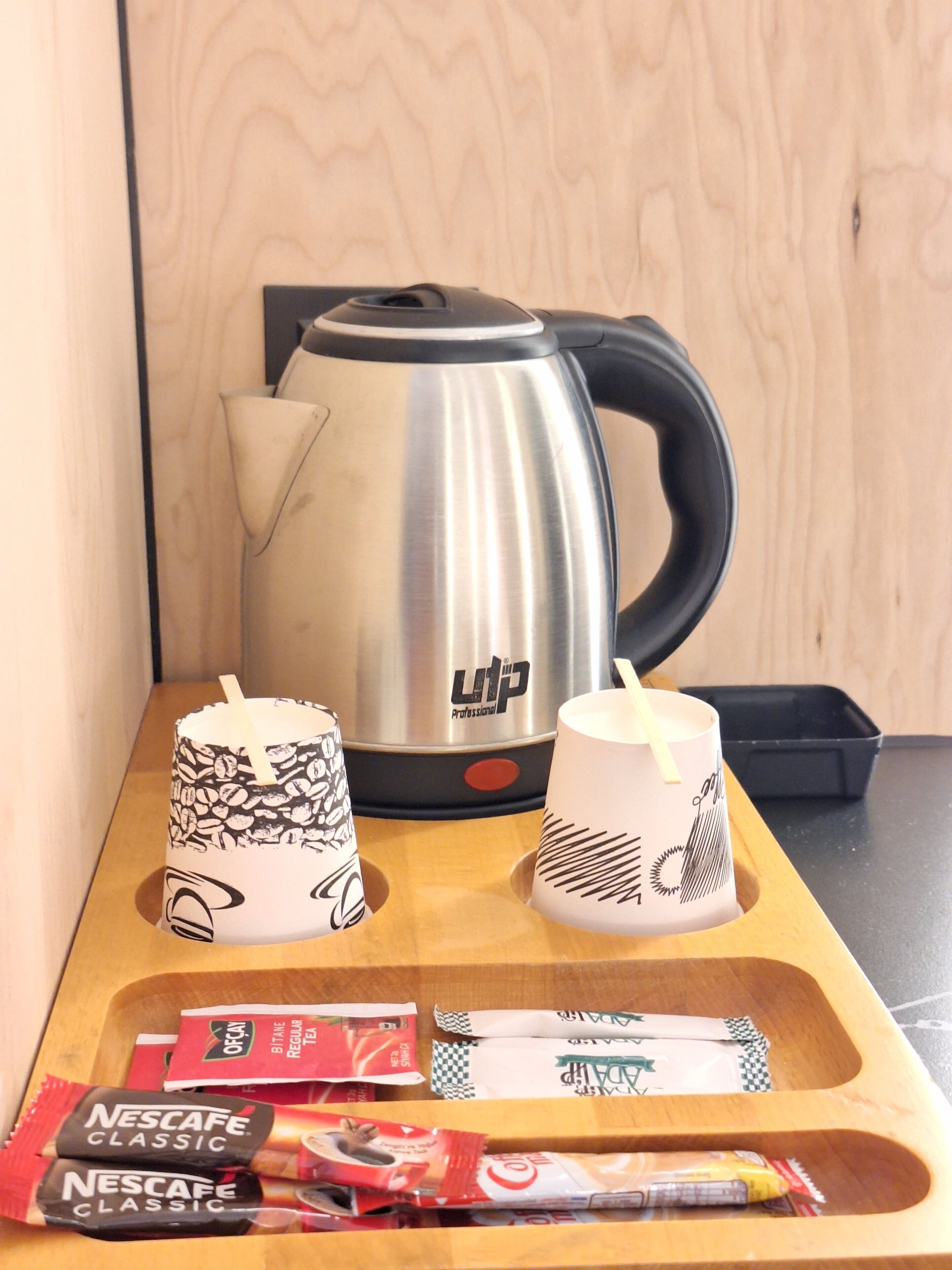 A wooden tray with a kettle, two cups, and packets of Nescafe Classic coffee.