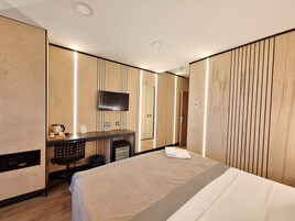 Quarto de hotel moderno com cama, escrivaninha com televisão de tela plana e painéis de madeira.
