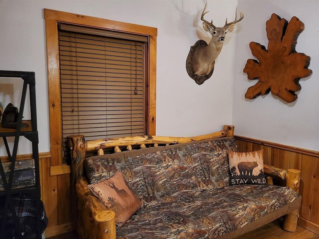Un canapé rustique en bois, orné d’un motif de camouflage, une tête de cerf accrochée au mur et un élément décoratif en bois.