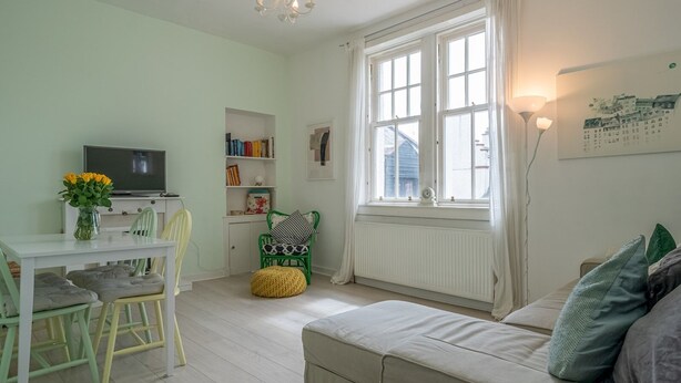 Un salon confortable avec un canapé, une table à manger et des chaises, une bibliothèque, un téléviseur et une fenêtre avec des rideaux.