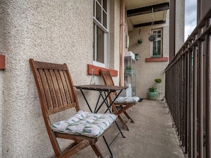 Un balcone con due sedie di legno, un tavolino, una pianta in vaso e un corrimano in metallo.