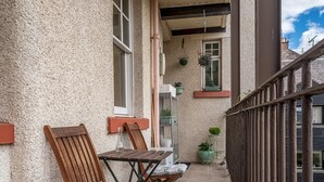 Un balcon avec des chaises et une table en bois, une plante en pot et une fenêtre donnant sur le ciel.