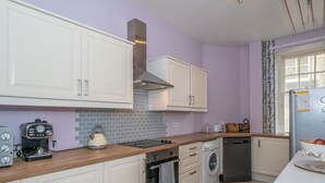 Une cuisine moderne avec des meubles blancs, un four encastré, un lave-linge et une machine à café.