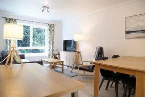 Une pièce moderne avec une table à manger en bois, un canapé et un téléviseur posé sur un meuble.