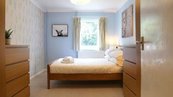 Un dormitorio ordenado con cama, cómoda, ventana con cortinas y una obra de arte colgada en la pared.