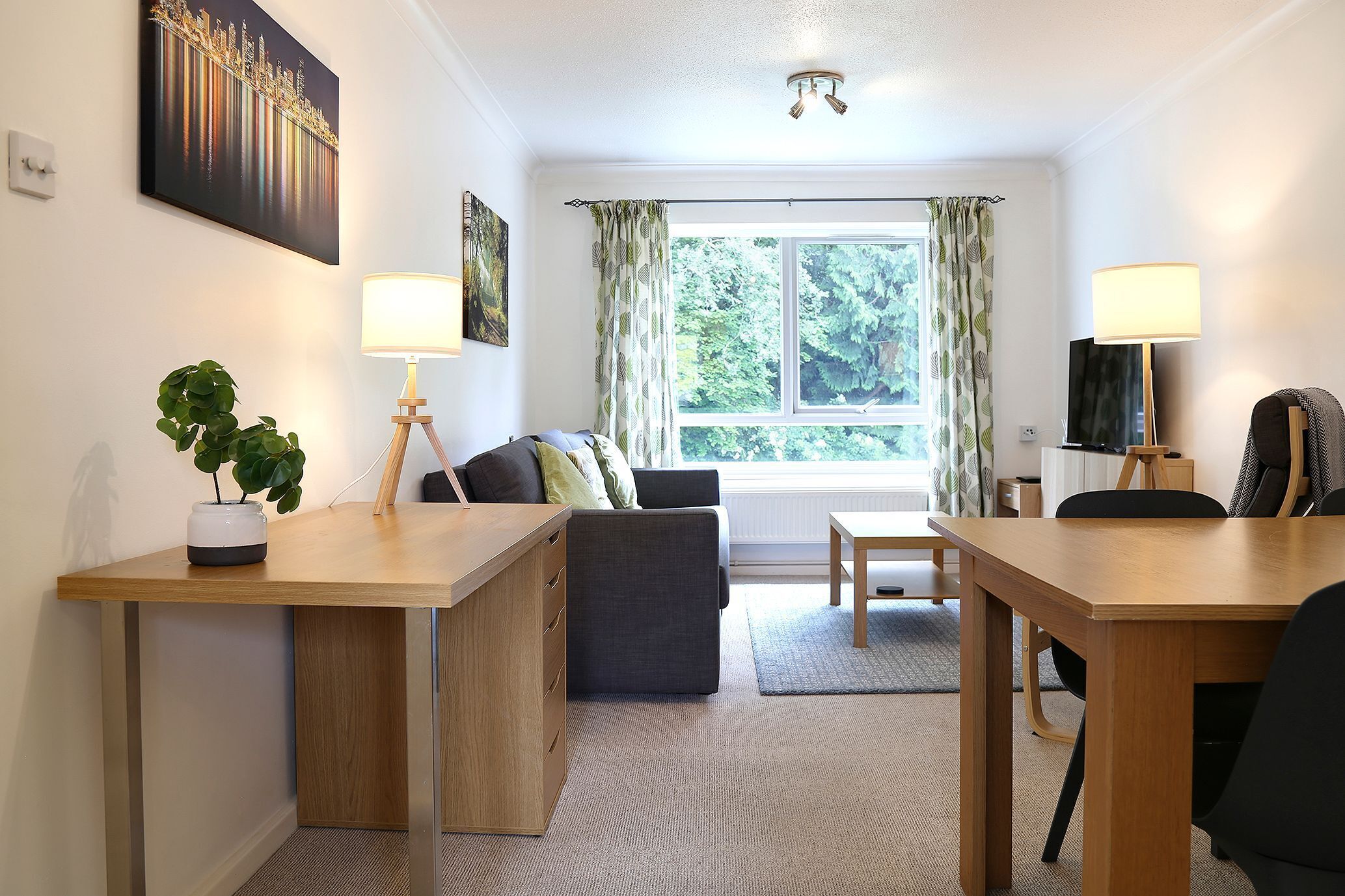 A modern room with a desk, sofa, and dining table. There is a window with curtains, a plant, and a lamp.