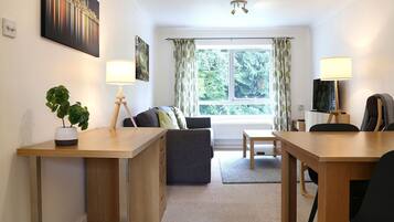 A modern room with a desk, sofa, and dining table. There is a window with curtains, a plant, and a lamp.