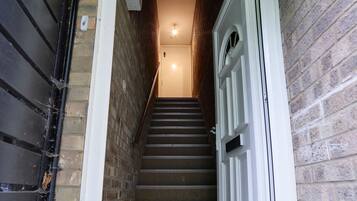 A narrow stairway leading to a door with a white frame, flanked by brick walls and a metal gate on the left.