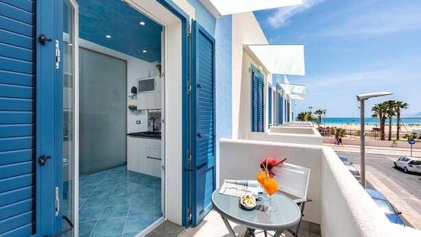 A balcony with a table set for two, overlooking a beach and a clear sky.