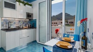 A modern kitchen with a blue tiled backsplash, white cabinets, and a large sliding glass door leading to a balcony with a mountain view.