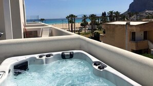 A hot tub on a balcony with a view of a beach and palm trees. - Bright and comfortable apartment with a sea-view terrace and private jacuzzi. (San Vito Lo Capo)