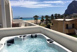 A hot tub on a balcony with a view of a beach and palm trees. - Bright and comfortable apartment with a sea-view terrace and private jacuzzi. (San Vito Lo Capo)