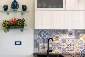 A kitchen with a tiled backsplash, a black faucet, and decorative items on shelves. - Apartment with swimming pool and terrace by the sea  (San Vito Lo Capo)