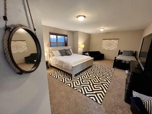 A bedroom with a bed, bedside tables, a dresser, a mirror, a window, and a patterned rug.