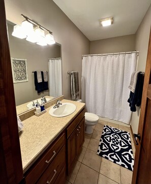 A bathroom with a sink, mirror, and toilet. There are towels hanging on the wall and a shower curtain.